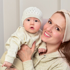 Mother and baby playing and smiling in knitted cap and sweater. Home interior.  Winter season.