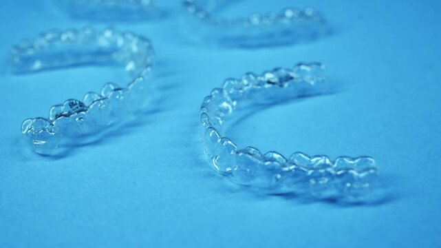 Invisible dental teeth brackets tooth aligners on blue background. Plastic braces dentistry retainers to straighten teeth.