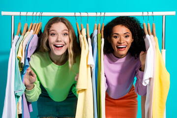 Two cheerful young women surrounded by colorful wardrobe in a bright turquoise room