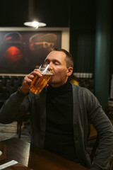 A relaxed man enjoys his beer in the stylish ambiance of the bar, fully embracing the leisure and enjoyment