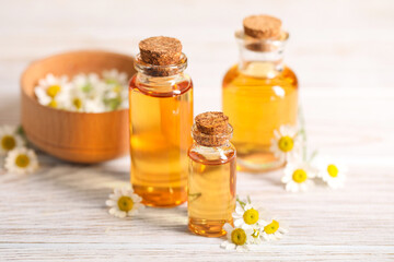 Bottles of essential oil and chamomile flowers on white wooden table, closeup