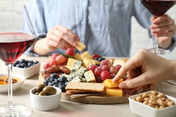 Women enjoying different snacks and wine during brunch at light grey table indoors, closeup