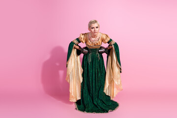 Fototapeta premium Elegant woman in medieval attire posing against pink background with dignified expression