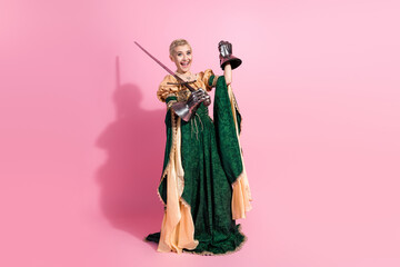 Fototapeta premium Charming woman in medieval attire holding a sword against a bright pink background, showcasing elegance and historical cosplay.