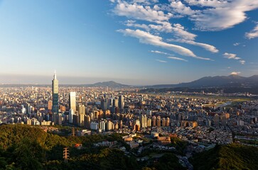 Fototapeta premium Aerial view of Downtown Taipei, capital city of Taiwan, with landmark 101 Tower standing among skyscrapers in Xinyi Financial District and Datun Mountain in background bathed in warm morning sunlight