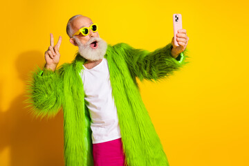 Fototapeta premium Elderly man in vibrant green fur and glasses taking a selfie against a yellow background