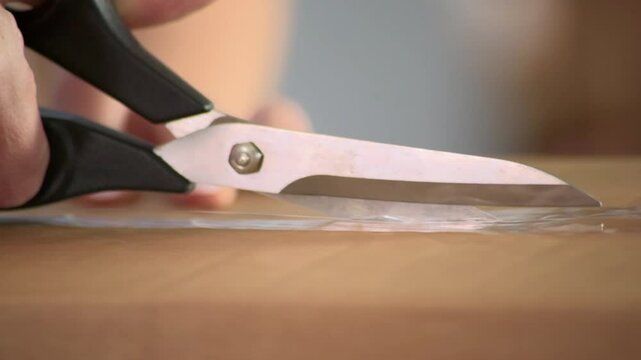 Hands with scissors open the cardboard delivery package by cutting the adhesive tape. Unboxing of online / mail order delivery with hands and scissors. Static, close up. 