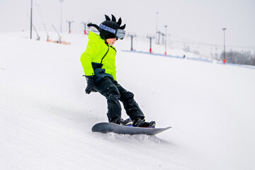 Young snowboarder in bright neon jacket riding downhill on snowy slope