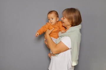 A grandmother proudly holds her young grandchild while both share a loving gaze. The cozy...