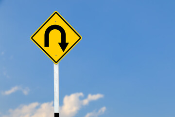 A black U turn symbol is prominently displayed on a bright yellow sign on blurred sky background.