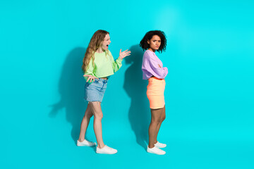 Two young women interacting dramatically on a vivid turquoise background, showcasing trendy casual...