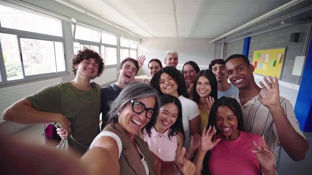 Cheerful selfie of young group of students waving and looking at camera with big smiles with their female teacher in the classroom, celebrating the back to school.