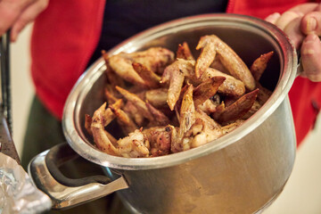 a man puts oven-cooked chicken wings into a pot