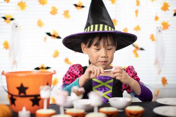 little girl wearing a a witch hat and making Halloween candy at home 