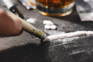 Snorting cocaine with a rolled-up dollar bill from a white powder line, white narcotic pills, an...