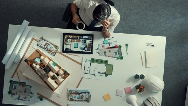 Top view of engineer drink coffee and thinking about house plan at meeting table with equipment and safety helmet scatter around. Aerial view of stressful manager looking at blueprint. Alimentation.