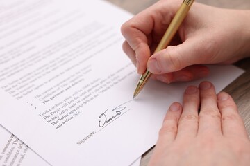 Woman putting signature on document at table, closeup