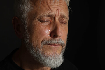 Sad senior man crying on black background, closeup. Space for text