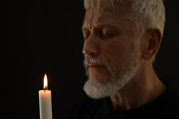 Sad senior man with burning candle crying on black background. Grieving loss