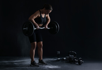 Woman training with barbell against black background