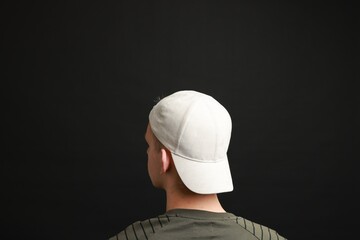 Man in stylish baseball cap on black background, back view. Mockup for design
