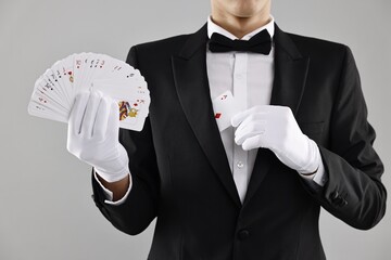 Illusionist hiding one playing card behind jacket lapel while showing deck on grey background,...