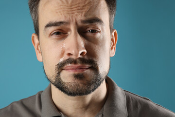 Sad man crying on light blue background, closeup