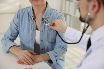 Cardiologist with stethoscope listening patient's heartbeat at desk in clinic, closeup