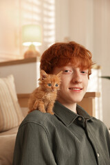 Redhead teenage boy with cute ginger kitten indoors