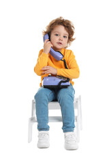 Cute little boy with telephone on step stool against white background