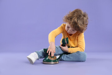 Cute little boy with old telephone on violet background