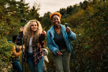 Two female hikers are enjoying a hike in a beautiful forest, with one pointing towards something interesting they've spotted along the trail © DusanJelicic