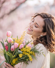 Naklejka premium International Women's Day celebration photo of a happy woman with spring flowers in soft sunlight