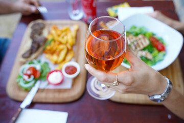 Woman raises her glass of rose wine in the air while dining opposite each other in a restaurant