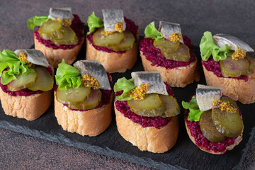 Bruschetta with herring, beetroot and pickled cucumber on slate plate