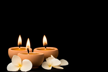 Three lit candles illuminating with flowers in foreground on a black background