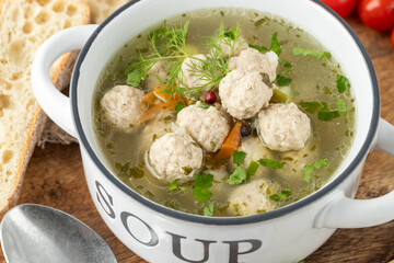 Meat balls soup in white bowl with herbs on wooden board. Ceramic pan with meatball soup with bread slices and spoon top view.
