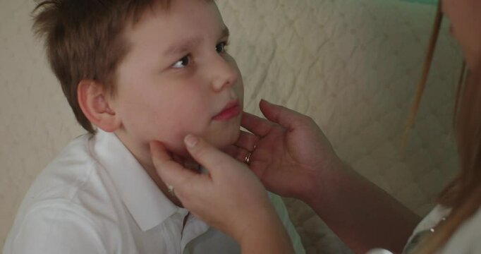 A female pediatrician gently palpates a little boy's neck, checking for lymph nodes or other signs of illness during a home visit. A doctor examines a sick child at home. Calling a doctor at home.
