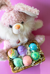 Cute bunny behind Easter eggs basket in pink background.