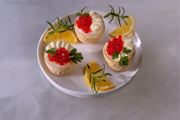 Tartlets with salmon caviar. In waffle cups with boiled egg and mayonnaise. On white flat plate with rim, with lemon wedges, parsley and rosemary leaves