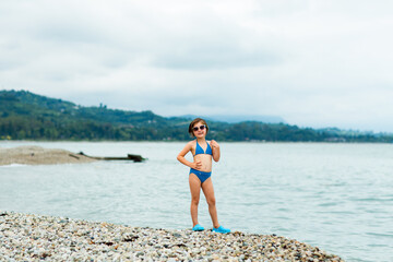 Fototapeta premium A small, beautiful girl in a blue swimsuit and sunglasses