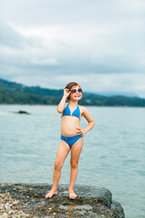 A small, beautiful girl in a blue swimsuit and sunglasses