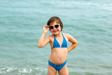 A small, beautiful girl in a blue swimsuit and sunglasses