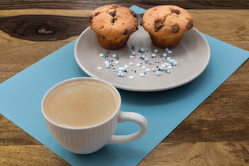 A plate of muffins and a cup of coffee sit on a table