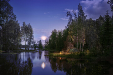 In the evening, a small tent is set up on the riverbank, and a bonfire is lit. The moon shines brightly in the sky, creating a peaceful and serene atmosphere.