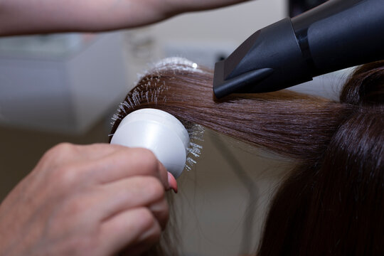 Close up of hairdressers hands drying long blond hair with blow dryer and round brush