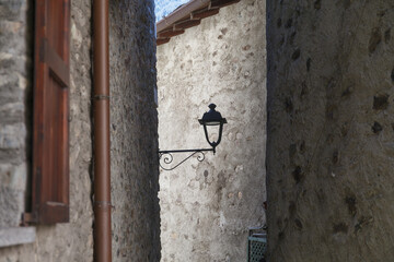 A vintage street lamp attached to a rustic stone wall of narrow old town street, featuring detailed ironwork and a weathered charm.