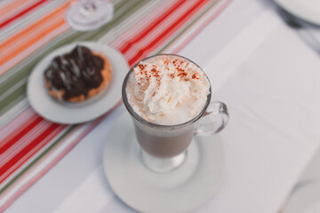 A chopped view of a cappuccino with a chocolate cupcake served on a table.