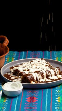 Vertical video, Mexican food, sesame seeds falling on a plate with chicken mole poblano enchiladas or enmoladas