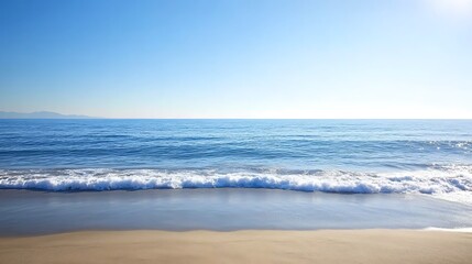 Obraz premium Serene ocean waves lapping a sandy beach under a clear blue sky